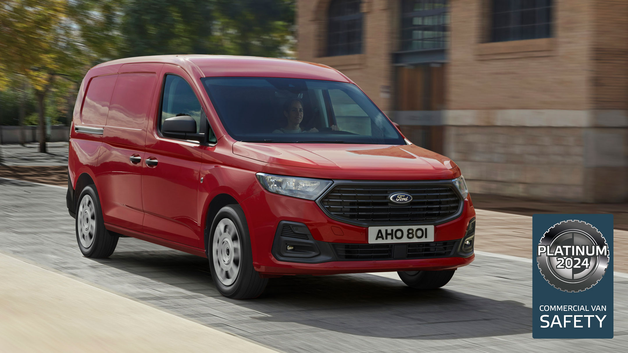 Ford Transit Connect Trend in Maple Red mit Kühlergrill und automatischen Scheinwerfern fährt eine Straße entlang. 