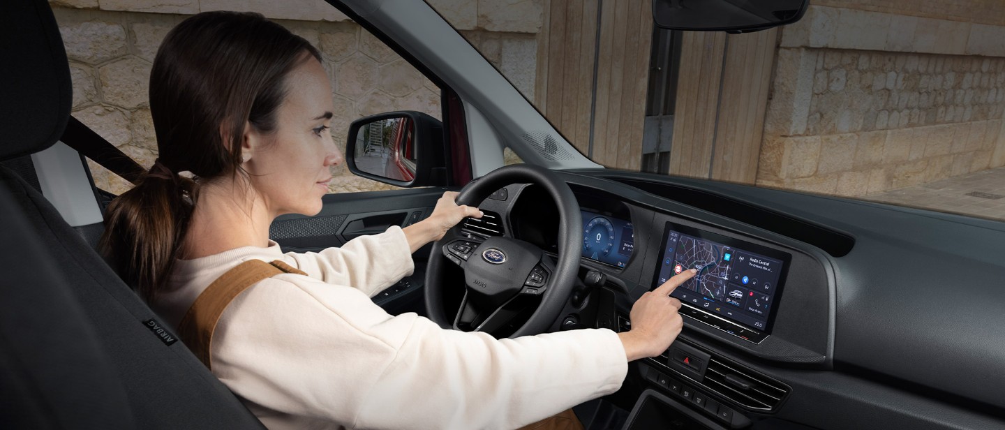 Eine Frau berührt den 10-Zoll-Touchscreen, während sie auf dem Fahrersitz Ford Transit Connect sitzt.