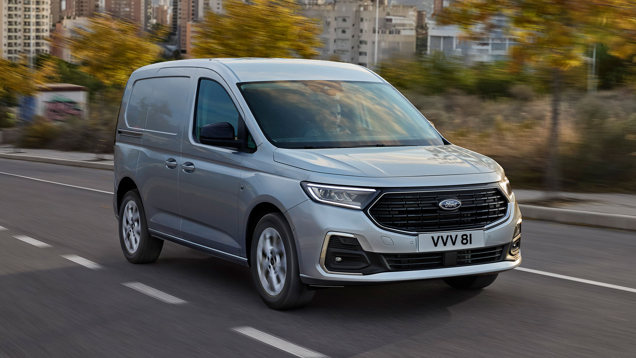 Ford Transit Connect Limited in Stardust Silver mit Chrom-Zierleisten und automatischen Scheinwerfern fährt auf einer Straße. 