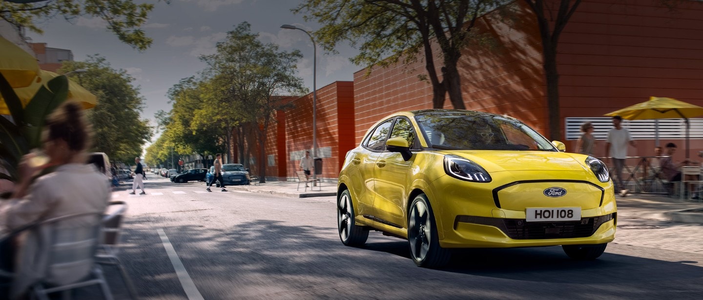 Frontansicht eines gelben elektrischen Ford Puma Gen-E®, der entlang einer Stadtstraße fährt.